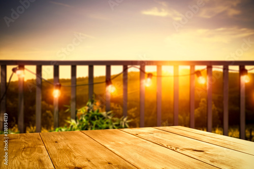 Fototapeta Naklejka Na Ścianę i Meble -  Wooden board of free space for your decoration. Blurred background of balcony and ladnscape of Tuscany.Small lights and orange color of sunset time. 