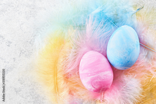 Happy easter concept. Pink and blue painted chicken eggs decorated with feathers and ribbons nest on light background close up with copy space