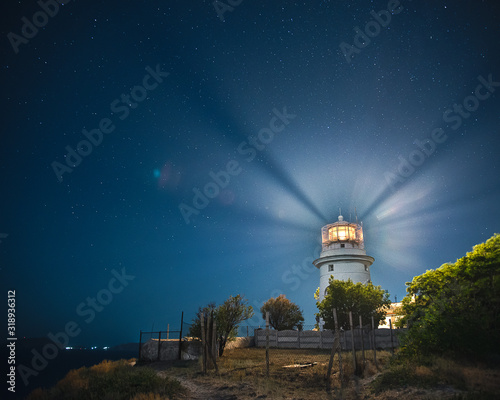 White sea lighthouse in Feodosia, Crimea on the Black Sea with rays of light under the night sky