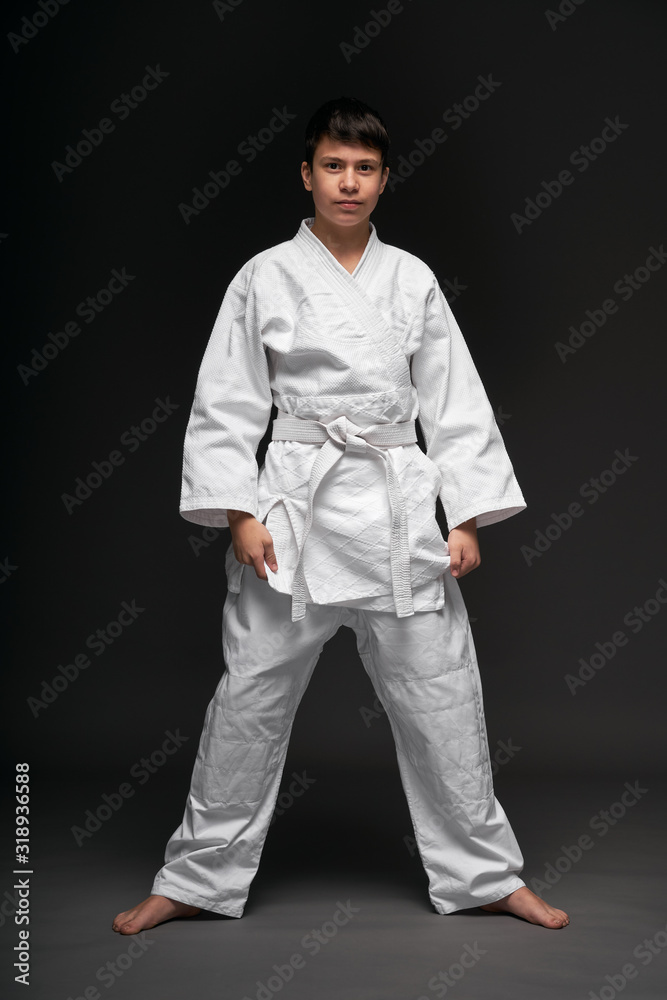 a teenager dressed in martial arts clothing poses on a dark gray background, a sports concept a teenager dressed in martial arts clothing poses on a dark gray background, a sports concept