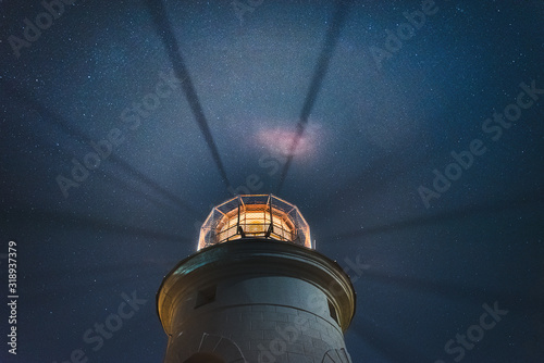 the sea lighthouse shines at night with bright rays of light against the background of the starry sky