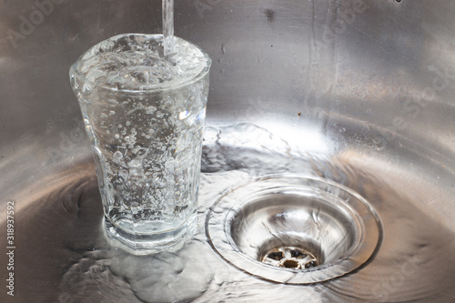 Water pours into a transparent glass in a metal sink