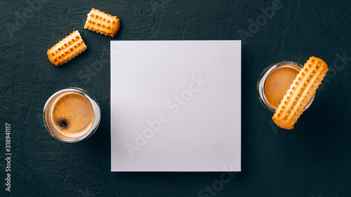 Two shots of espresso in glass transparent cups,bisuits and white square paper card for text on a dark stone background photo