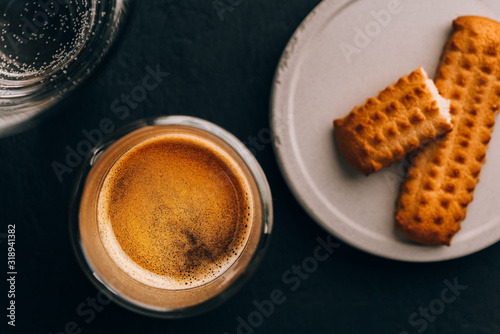 One portion of espresso in glass transparent cups,bisuits and water on a dark stone background photo