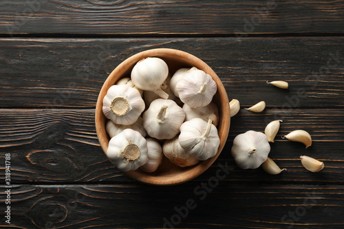 Wooden bowl of fresh garlic bulbs, slices on wooden background, top view. Space for text