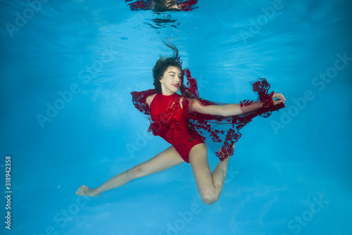 Young beautiful girl in a red dress posing underwater in the pool
