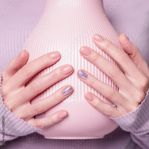 Beautiful female hands holding pink vase on the pale violet background. Manicure with pink color nail polish with shiny design  nude manicure. Copy space