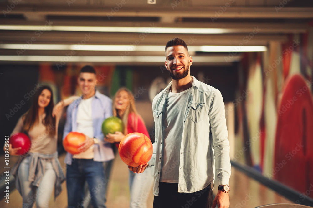 Beautiful group of young people posing in a bowling alley with a ball in their hand