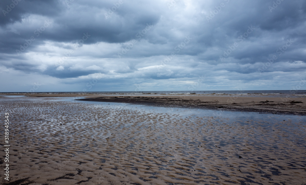 Obraz premium Reflection of clouds in a small lehman on the sandy shore of the Baltic Sea in Jurmala in cloudy weather.