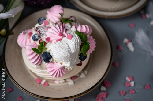 Meringue cake Pavlova with berries and mint leaves. St. Valentine's Day breakfast with flowers and coffee. Beautiful and delicious white and pink cake with hearts made of sugar on grey background