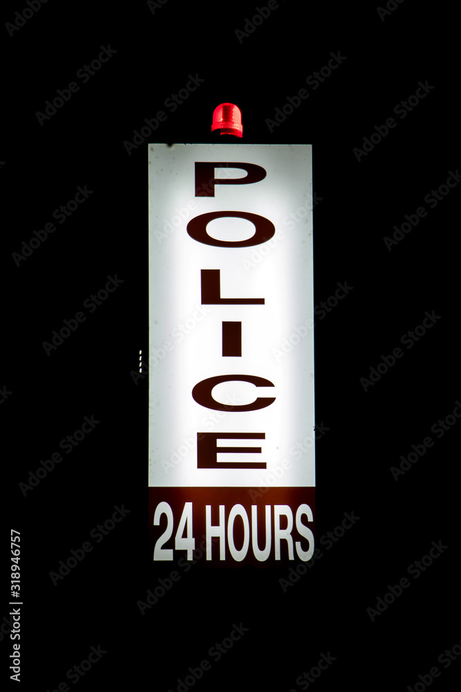Illuminated police sign with a red flashing beacon at a police station lights in the night. Nonstop police service. Illuminated police sign with a red flashing beacon at a police station lights in the night. Nonstop police service.