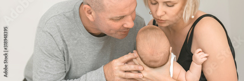 Parents mother and fother are holding their little baby and looking on him, panorama view, banner photo