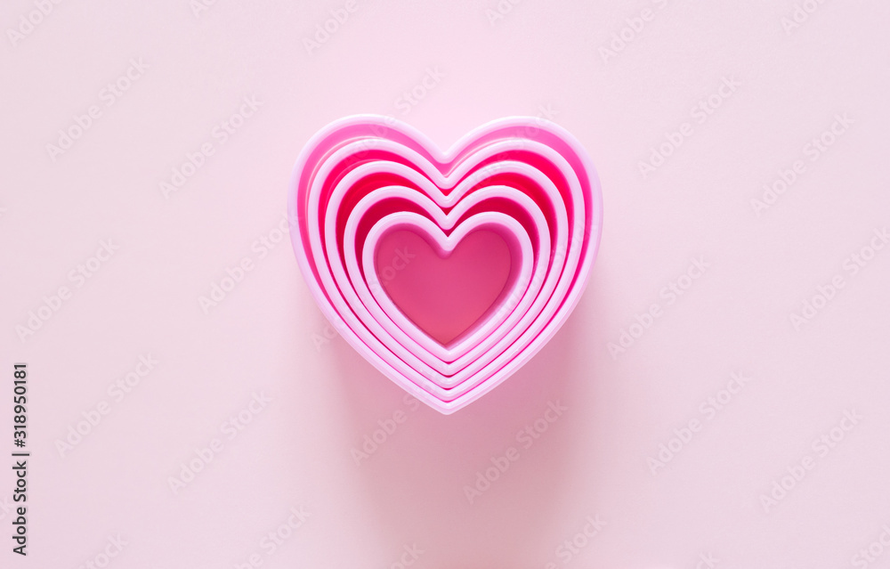 Pink plastic cookie cutters in the shape of hearts on a gentle pastel backdrop. Composition with forms for valentines greeting card, cover or packaging, top view.