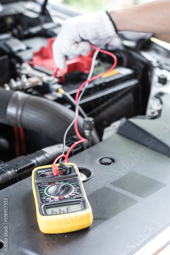 Thai young man is checking the voltage level in a car battery using multimeter. Selective focus at multimeter.