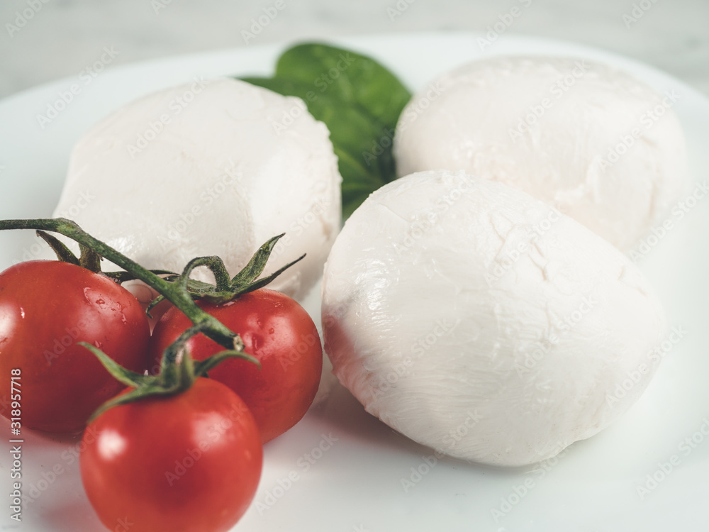 three mozzarella and cherry tomatoes on plate. White fresh cheese . Healthy dinner. Traditional italian ingredients .