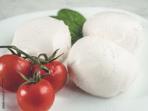 three mozzarella and cherry tomatoes on plate. White fresh cheese . Healthy dinner. Traditional italian ingredients .