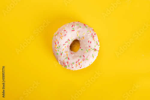 Glazed donut with colorful sprinkles on yellow background. Sweet pastries for Fat Thursday.