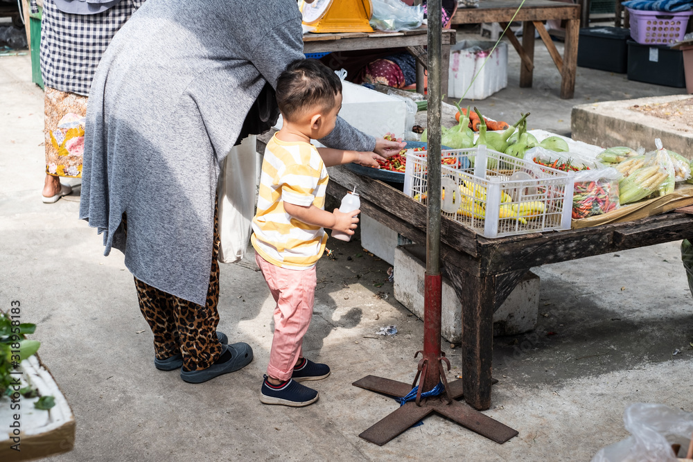 Obraz premium Thai young muslim mother bring her baby boy going to local market for buying vegetable.