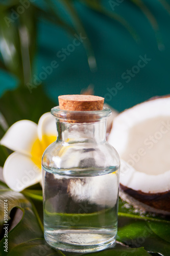 Coconut oil in a bottle with coconuts, flower Plumeria frangipani and green palm tree leaf. Healthy Food, skin care concept.