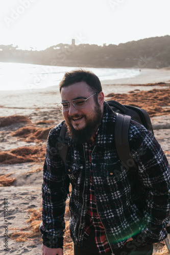 young man smiling on the beach with glasses and beard at sunset © Gragon