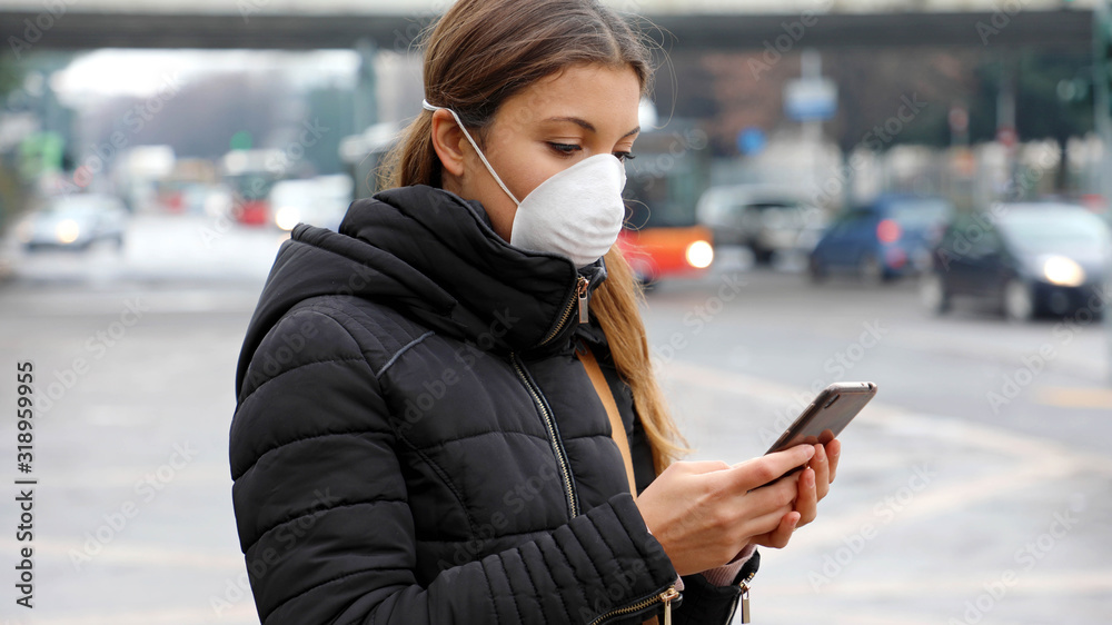 Plakat COVID-19 Pandemic Coronavirus Application - Young Woman Wearing Face Mask Using Smart Phone App in City Street to Aid Contact Tracing in Response to the 2019-20 Coronavirus Pandemic