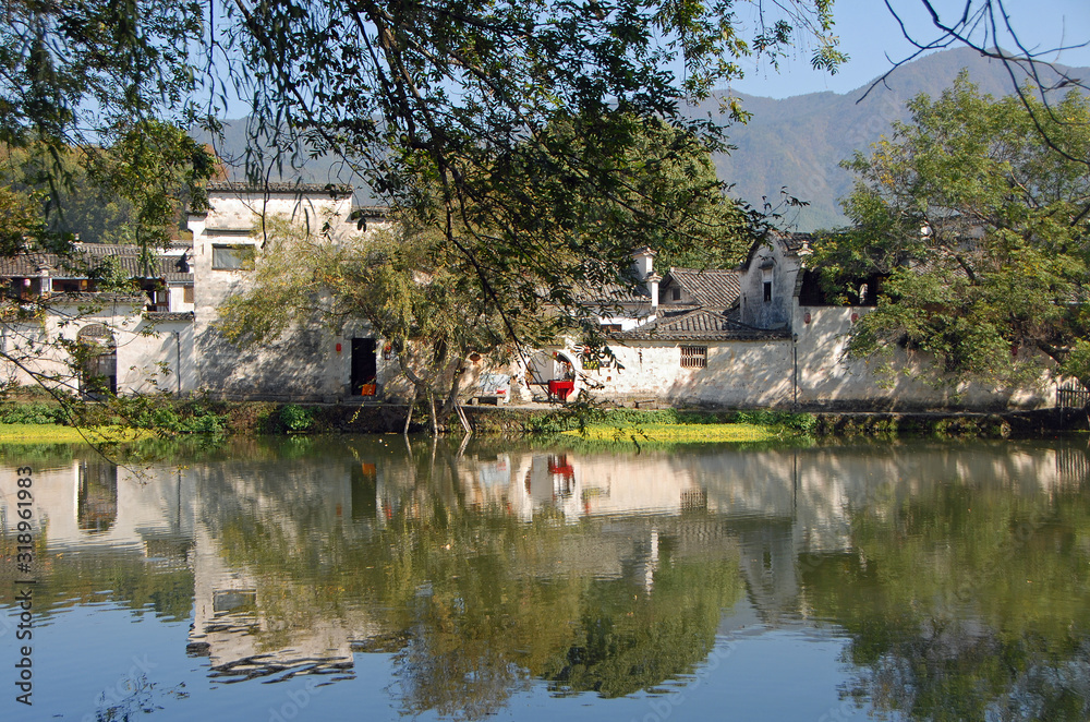 Obraz premium Hongcun Ancient Town in Anhui Province, China. A beautiful view of the old buildings of Hongcun with their reflection in the water of Nanhu Lake and trees. The pretty, ancient town of Hongcun in China