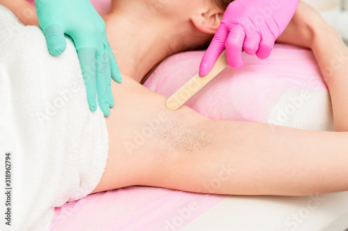 Female getting waxing armpit by beautician in a beauty salon, close up.