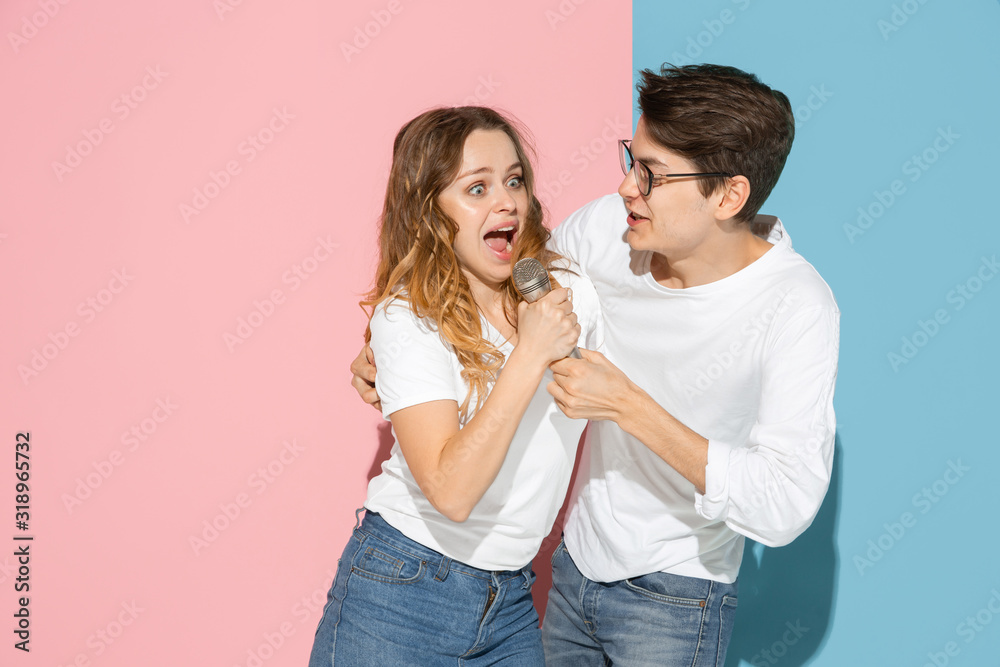 Singing song together. Young and happy man and woman in casual clothes on pink, blue bicolored background. Concept of human emotions, facial expession, relations, ad. Beautiful caucasian couple.