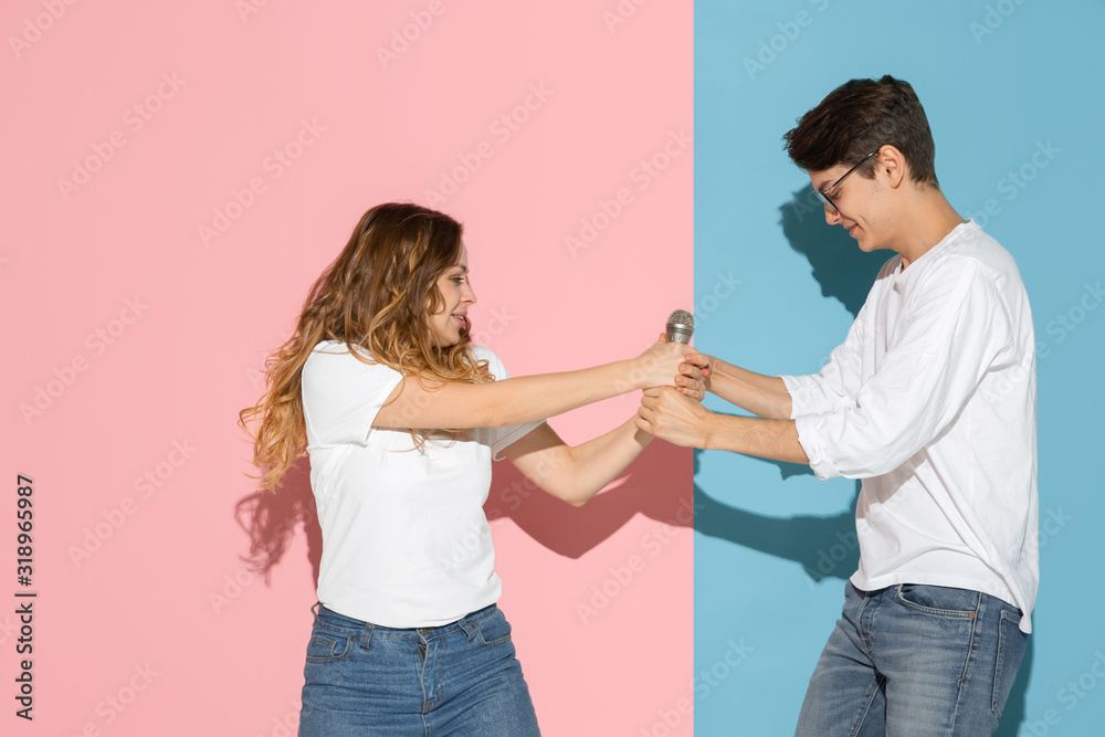 Fighting for speaker. Young and happy man and woman in casual clothes on pink, blue bicolored background. Concept of human emotions, facial expession, relations, ad. Beautiful caucasian couple. Fighting for speaker. Young and happy man and woman in casual clothes on pink, blue bicolored background. Concept of human emotions, facial expession, relations, ad. Beautiful caucasian couple.