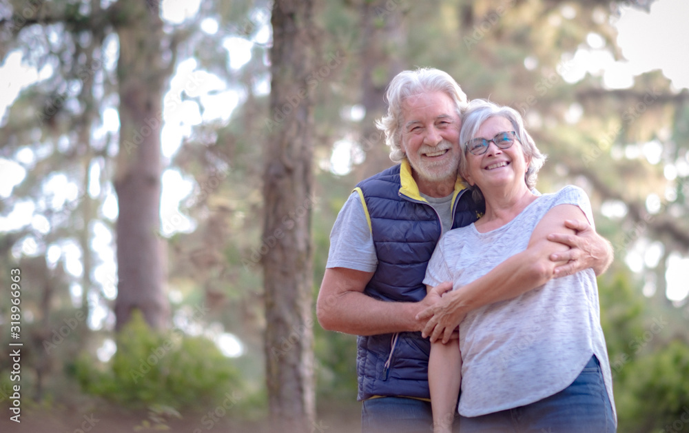 An elderly pretty couple outdoors in a green forest. Two senior adult people celebrate Valentine's Day with joy and hugs