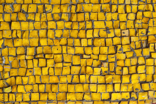 Texture of a wall made of small stones. The wall is clad with yellow granite cubes.