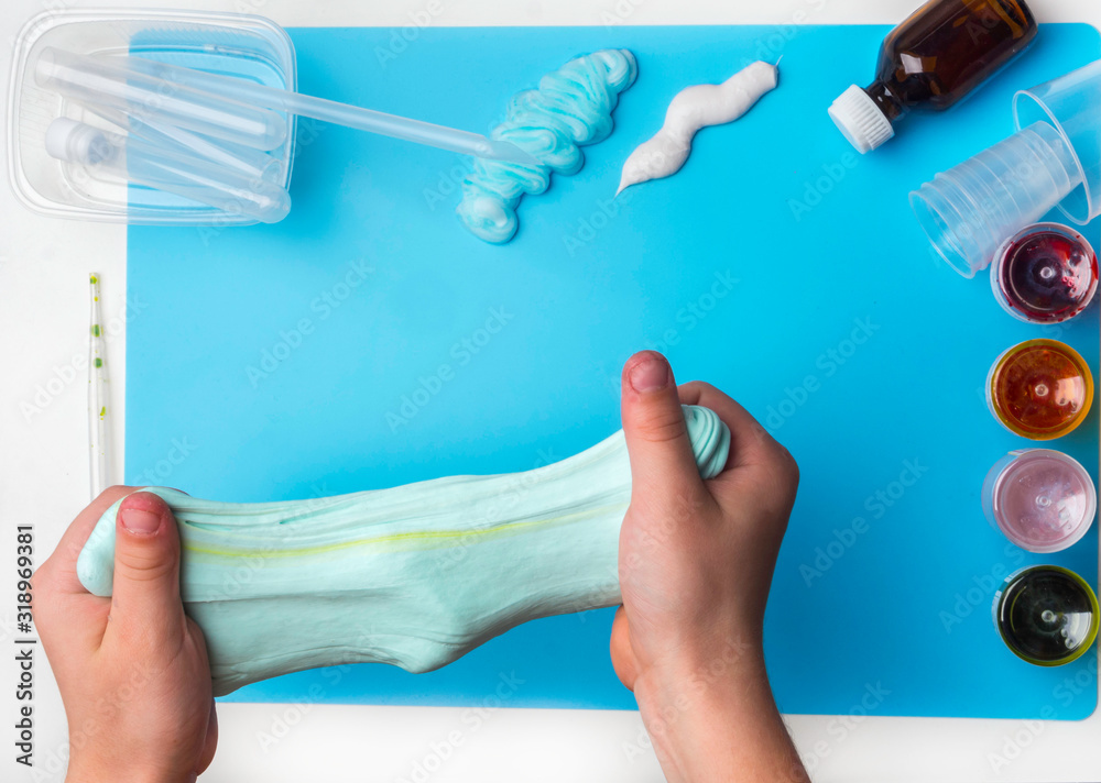 Components to make slime. Child education concept. On blue surface slime, toothpaste, shaving foam, decorative accessories, color paints on blue background Components to make slime. Child education concept. On blue surface slime, toothpaste, shaving foam, decorative accessories, color paints on blue background