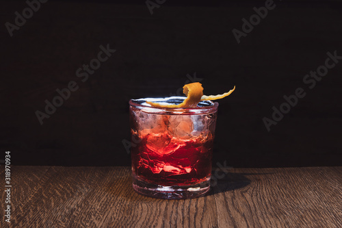 Cracked whisky glass. Red alcohol cocktail with beautiful backlight on a wooden table. Served with ice and orange peel. Boulevardier or Negroni. Bar with low light. Copy space.