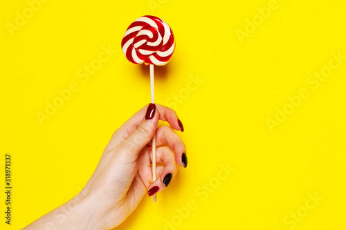 Candy in a female hand on a yellow background close-up.