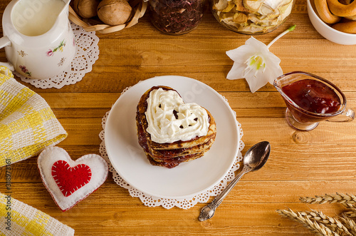 Fritters, pancakes in the form of hearts with jam and whipped cream on a light wooden background with a red heart, a romantic breakfast for Valentine's Day. Mothers Day. Cooking