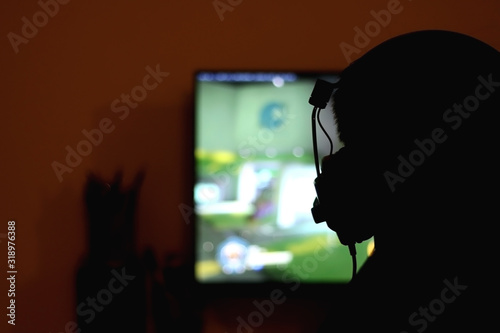 Silhouette of an unrecognizable man with headset playing computer games. Selective focus.