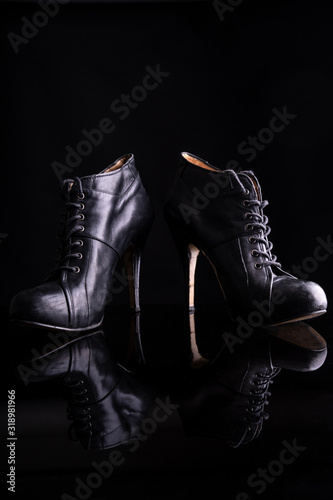 Black women's ankle boots on a black surface reflecting the ankle boots. The photo is taken in a photo studio with flash light illuminating the boots and on a black background © Supermelon