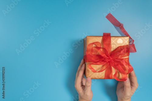Fototapeta Naklejka Na Ścianę i Meble -  Someone hands holding a big gift box tied with red ribbon over blue background