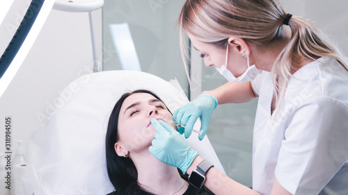Beautician hands making botox injection in female lips. The doctor cosmetologist makes lip augmentation procedure.
