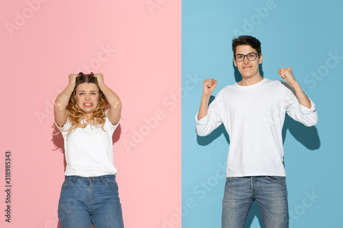 Oppositive emotions. Young and happy man and woman in casual clothes on pink, blue bicolored background. Concept of human emotions, facial expession, relations, ad. Beautiful caucasian couple. photo