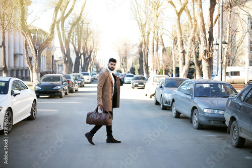 Handsome Indian man in elegant formal suit walking on city street with bag.