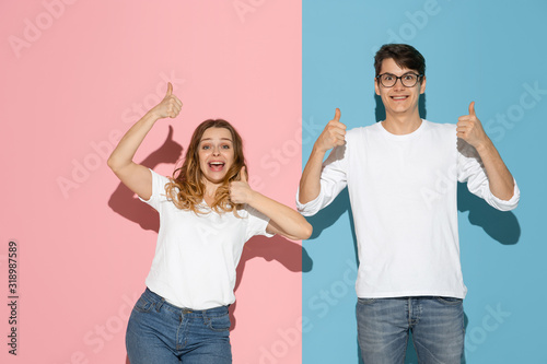 Thumbs up. Dancing. Young and happy man and woman in casual clothes on pink  blue bicolored background. Concept of human emotions  facial expession  relations  ad. Beautiful caucasian couple.