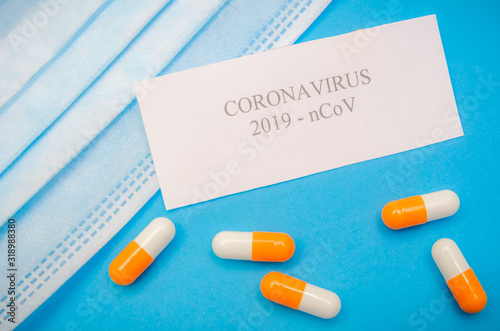 Medical mask, orange and white capsules on a blue background and the inscription coronavirus on a white sheet of close-up. First aid, care during illness. Background