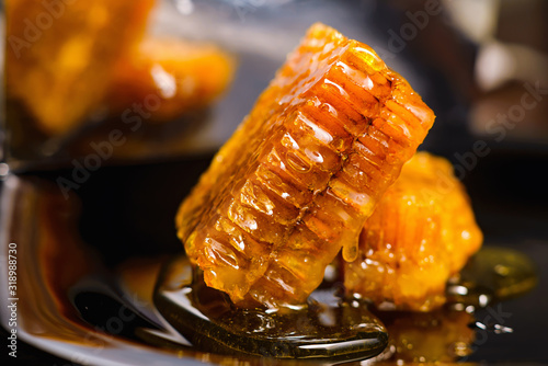 Honey close-up. Amber sweet honey in honeycomb. Square cut piece of honeycomb with honey on a black background