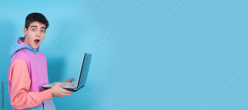 young teenage man or student with laptop isolated on background with surprise or success expression - obrazy, fototapety, plakaty 