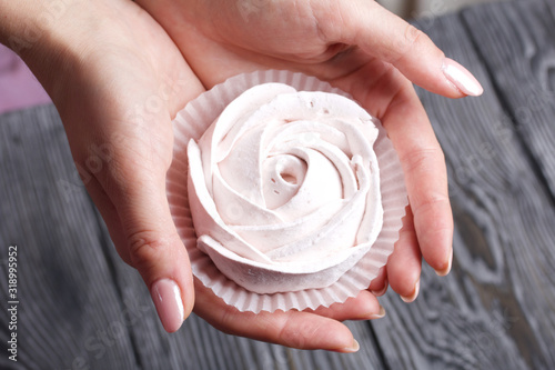 Marshmallows in the form of a rose in the palms of a woman. Against the background of brushed pine boards painted in black and white. photo