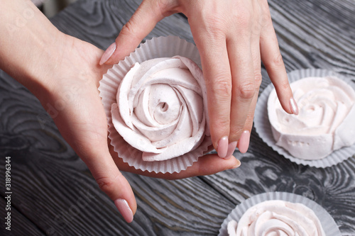 Marshmallows in the form of a rose in the palms of a woman. Against the background of brushed pine boards painted in black and white. photo