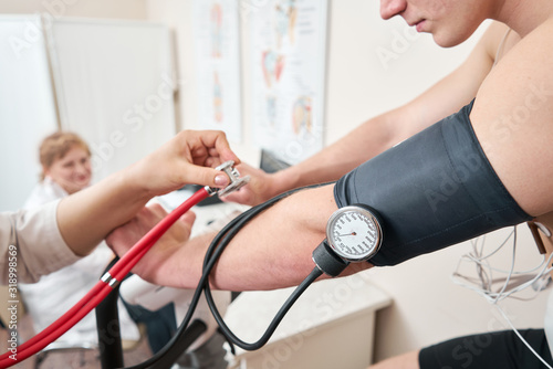 The nurse measures arterial tension. Man patient, pedaling on a bicycle ergometer stress test system for the function of heart checked. Athlete does a cardiac stress test in a medical study photo