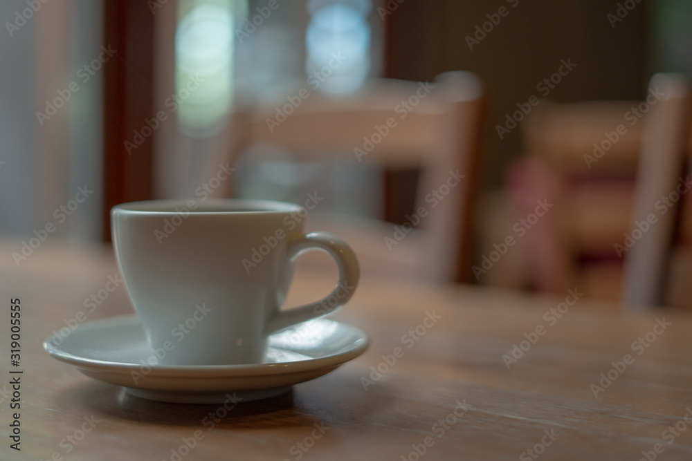 The white ceramic coffee cup with coaster is placed on a brown wooden base on the back, naturally a blurred background. The white ceramic coffee cup with coaster is placed on a brown wooden base on the back, naturally a blurred background.
