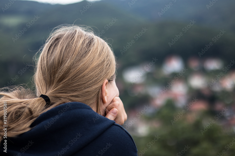 A young blonde woman looking out on to a scenic view.